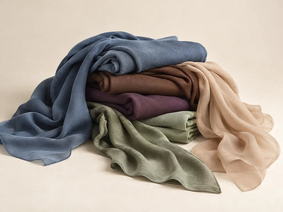 Pile of Wazi Empire hijabs in different fabrics, from matte to sheer chiffon, in blue, brown, purple, sage green and beige