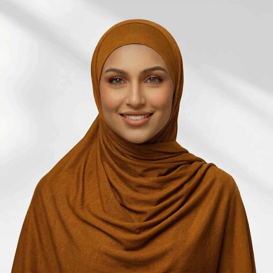 Woman wearing a gold jersey hijab in a warm caramel tone, draped for full chest coverage