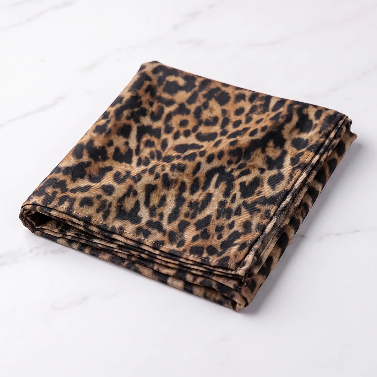 Folded leopard print modal hijab with black and cognac rosettes on white marble