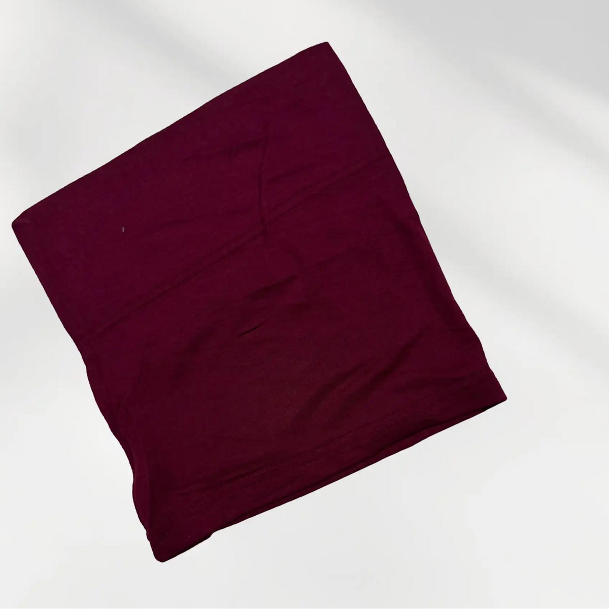 Maroon hijab cap folded flat, showing the tube shape and stretch band that sits at the hairline