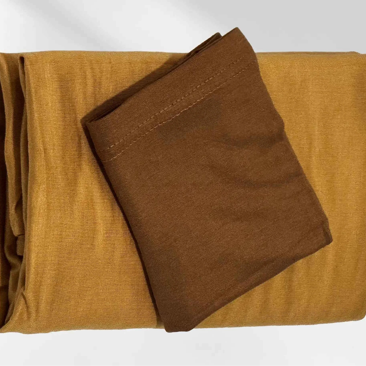 Yellow jersey hijab folded with its brown hijab cap resting on top, shown as a complete set